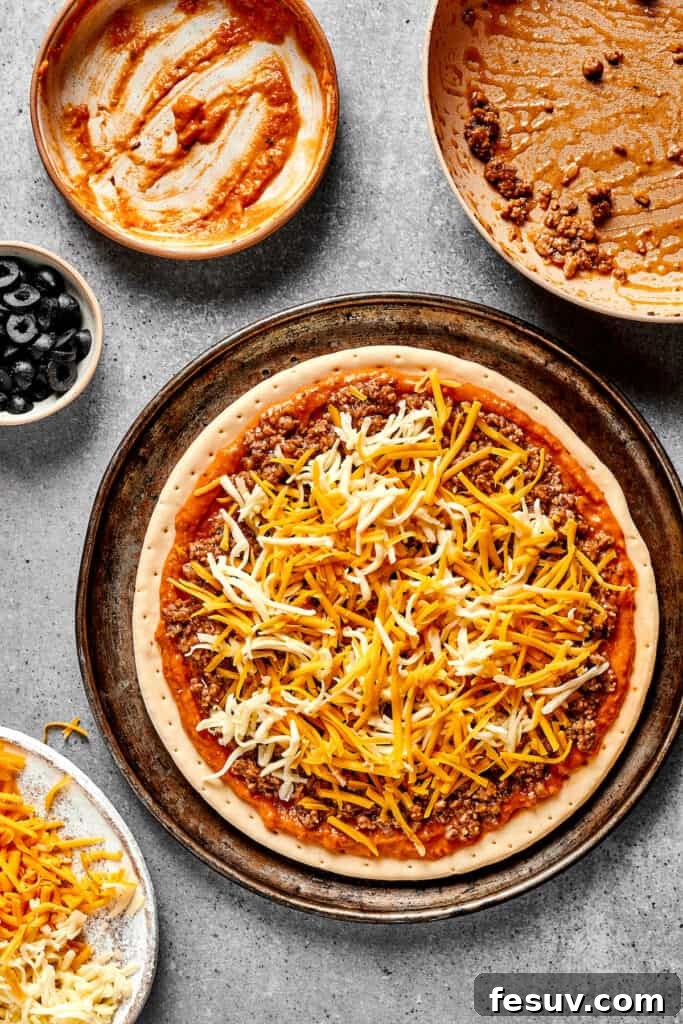 Tex-Mex Fiesta Pizza 6 A pizza crust beautifully layered with refried bean sauce, seasoned beef, and a generous amount of shredded cheese, ready for the oven.