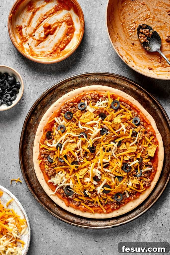 Finishing touches: black olives are sprinkled over an unbaked taco pizza, adding a savory note before baking.