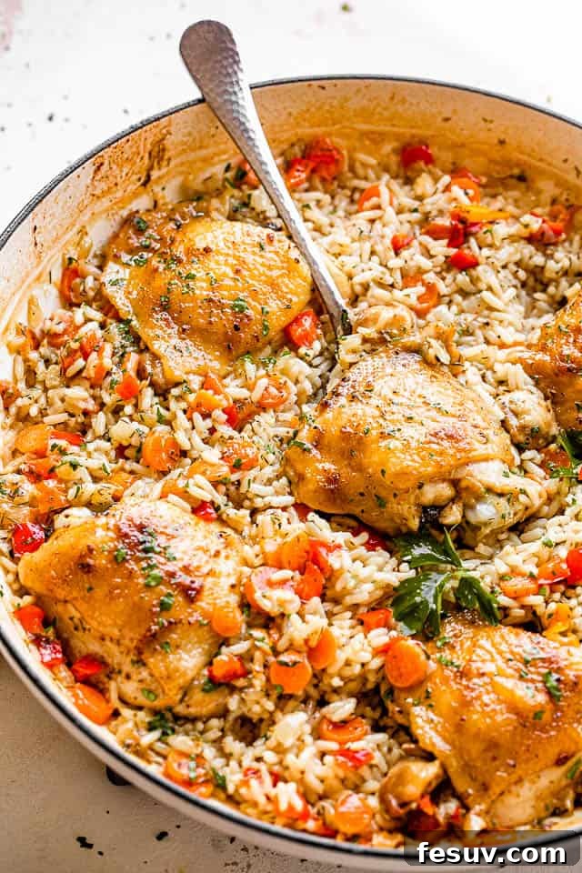 This one pot chicken and rice recipe is a whole meal - tender, pan seared chicken thighs, sautéed veggies, and creamy rice. So good! scooping out chicken thighs set on a bed of rice inside a white skillet