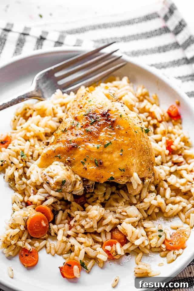 This one pot chicken and rice recipe is a whole meal - tender, pan seared chicken thighs, sautéed veggies, and creamy rice. So good! skin-on chicken thighs served over rice in a white plate with fork on the side