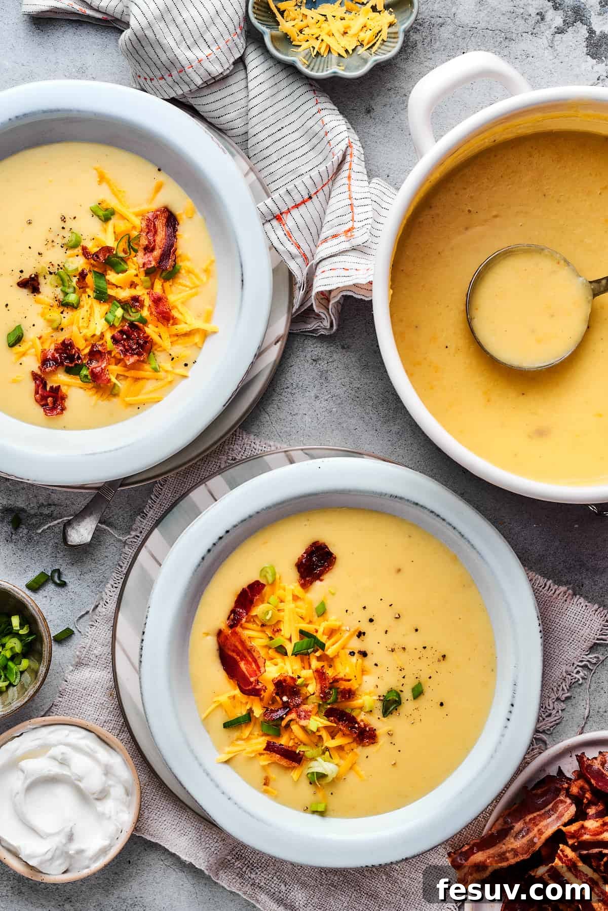 Ultimate Cheesy Bacon Potato Soup 11 A large pot of freshly made loaded baked potato soup sits beside two individual bowls, each perfectly garnished and ready to be served.