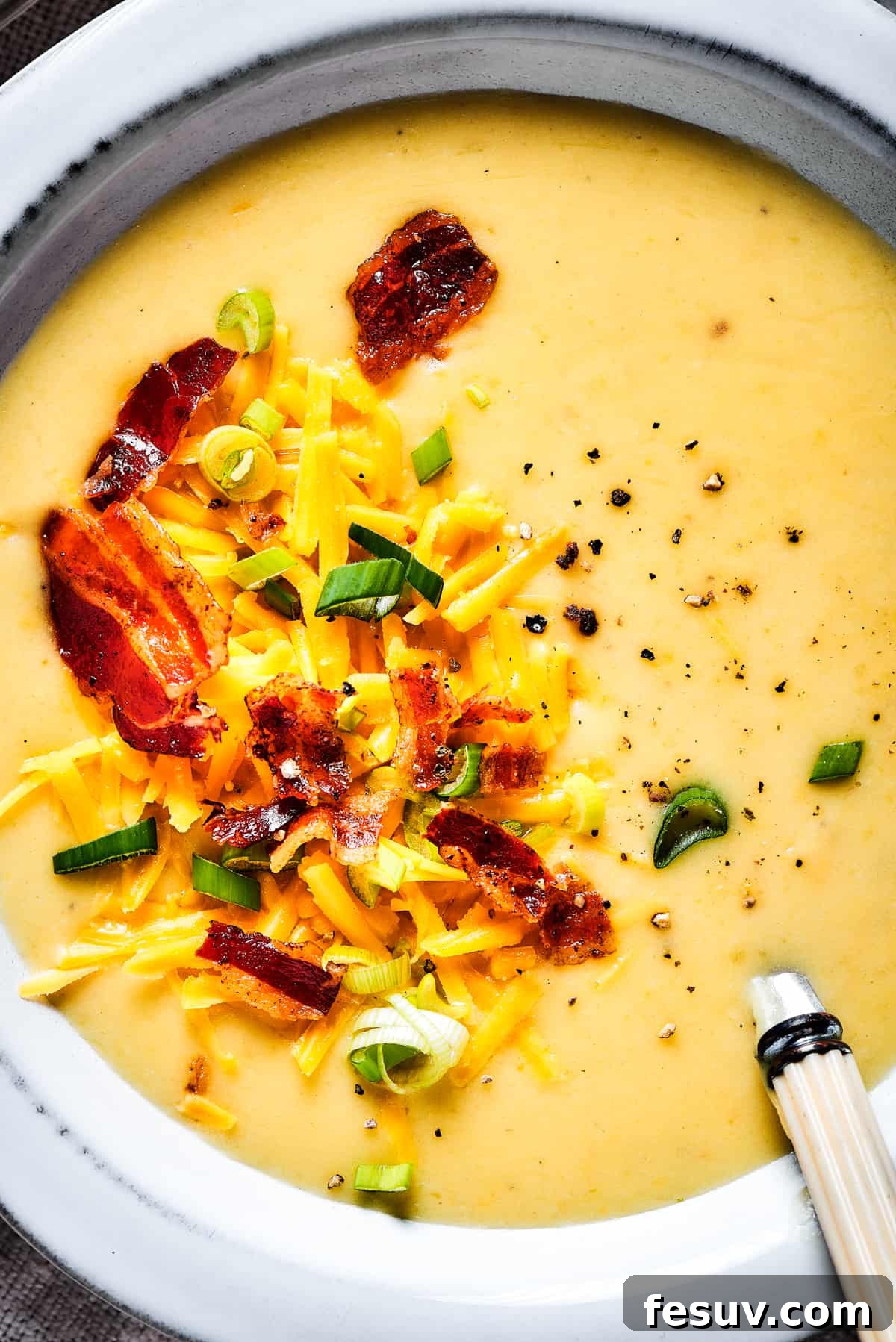 Ultimate Cheesy Bacon Potato Soup 3 Close-up view of a steaming bowl of loaded baked potato soup, generously garnished with crumbled bacon, vibrant green onions, and shredded cheese.