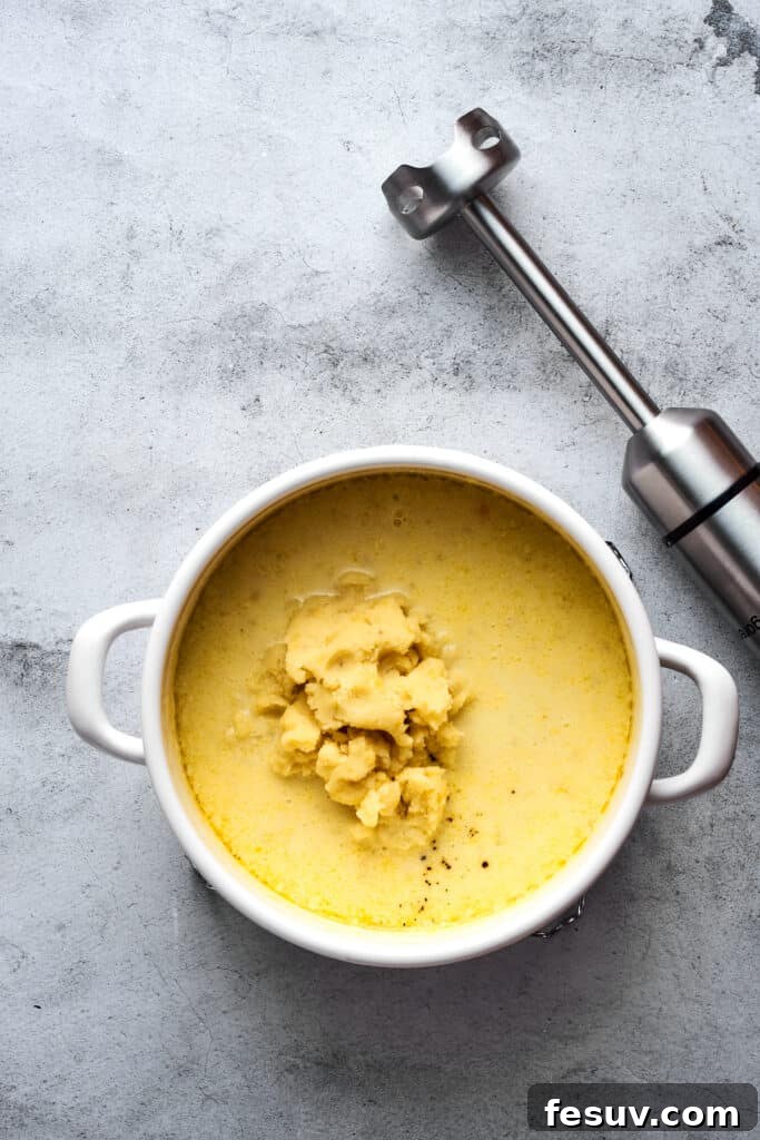Ultimate Cheesy Bacon Potato Soup 9 A large pot of creamy potato soup with an immersion blender resting beside it, ready to achieve a silky smooth texture.