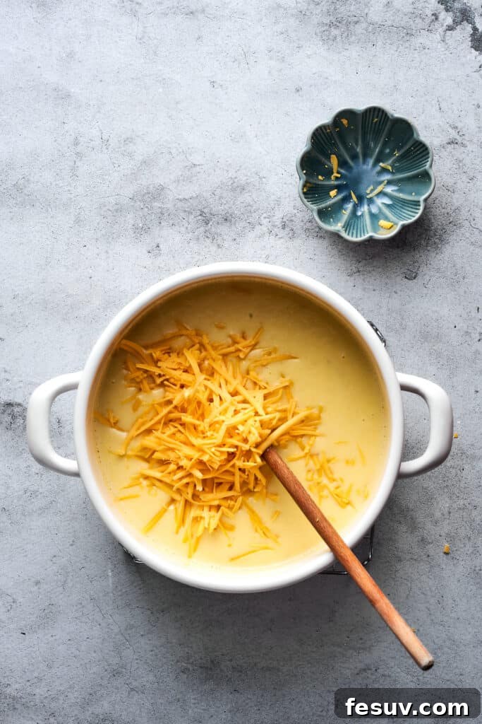 Ultimate Cheesy Bacon Potato Soup 10 A generous amount of shredded cheddar cheese being stirred into a pot of warm, creamy potato soup, melting into the delicious blend.