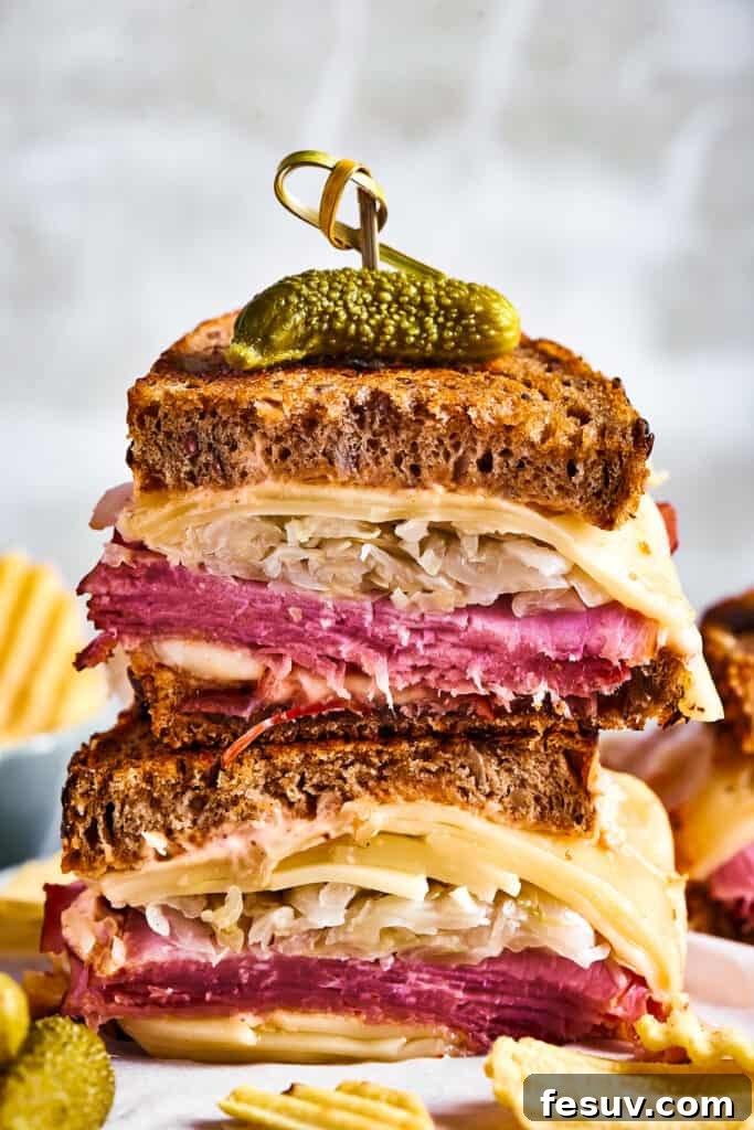 Two halves of a perfectly grilled Reuben sandwich, stacked and held together with a decorative skewer, revealing gooey melted cheese, savory corned beef, and tangy sauerkraut, served alongside a crisp pickle spear.