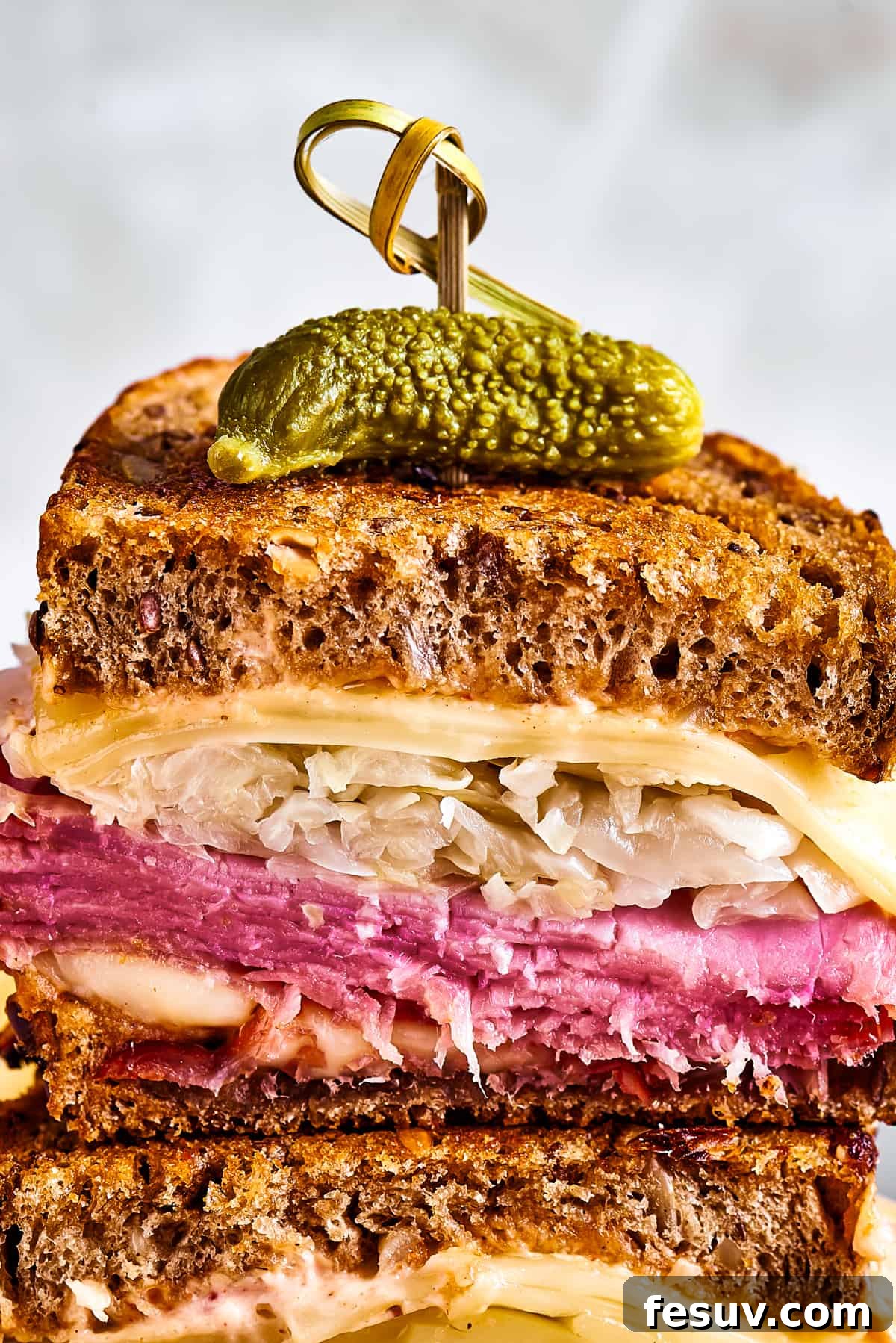 A perfectly assembled Reuben sandwich, halved and elegantly stacked, held together with a decorative skewer, showcasing its appetizing layers against a gently blurred background, ready to be enjoyed.
