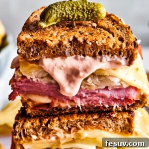 Two Reuben sandwich halves with Russian dressing dripping from one, showcasing melted Swiss cheese and layers of corned beef and tangy sauerkraut, ready to be enjoyed.