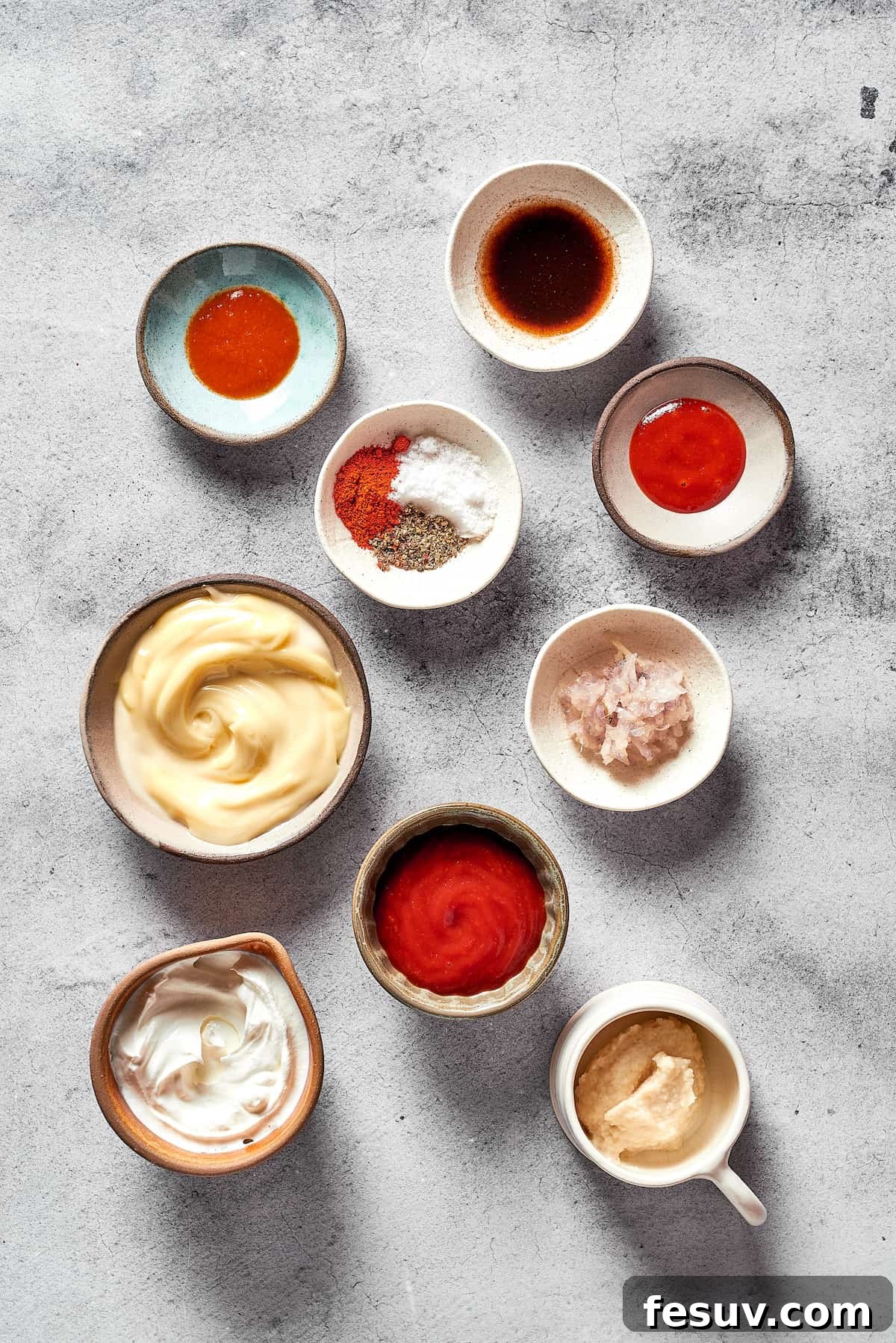 All the distinct ingredients required for homemade Russian dressing are neatly measured and displayed in individual white dishes, including mayonnaise, sour cream, ketchup, hot sauce, shallots, and various spices.