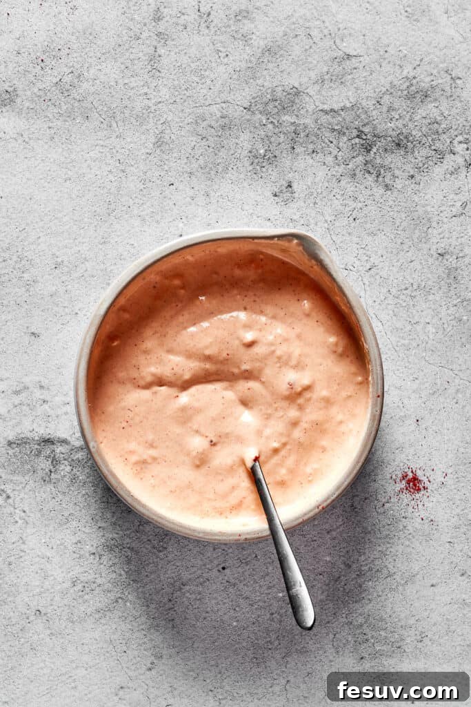 A close-up shot of freshly prepared Russian dressing, vibrant with its characteristic orange-pink hue, presented in a small bowl and ready to be chilled to perfection.