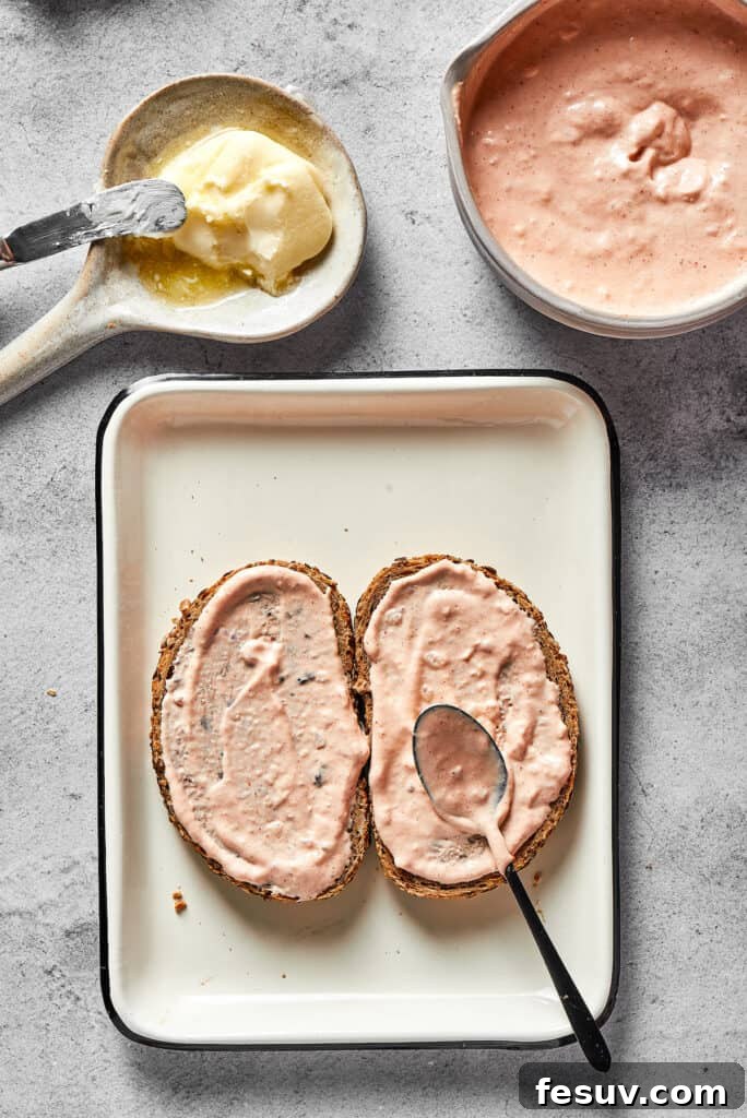A generous, creamy layer of homemade Russian dressing being spread evenly onto the unbuttered side of a slice of rye bread, forming the flavorful base for the sandwich fillings.