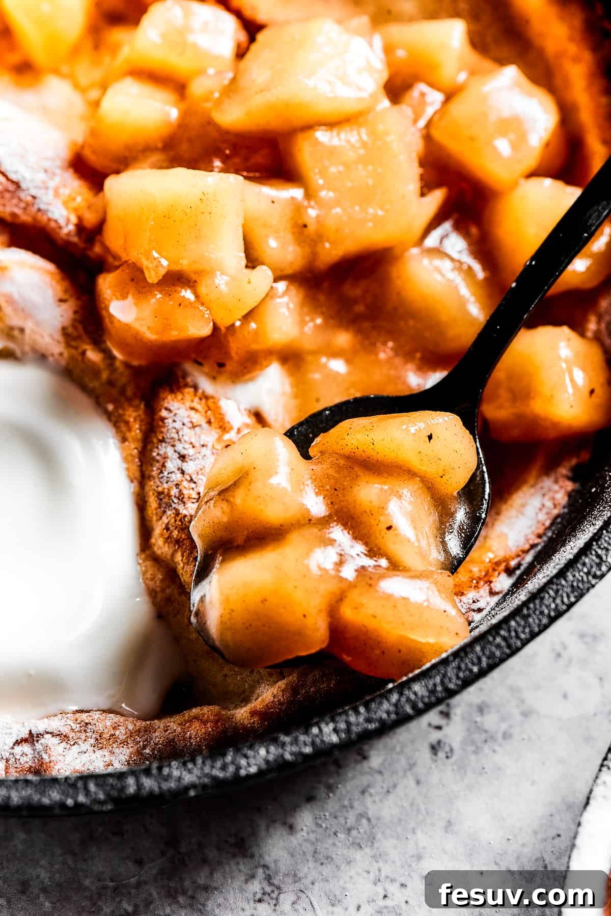 spooning apple pie filling on top of a dutch baby pancake.