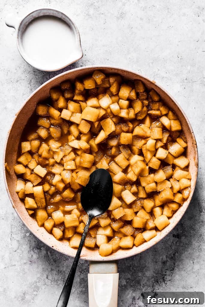 cooking diced apples in a skillet, with a dark spoon set inside the skillet, and a cup of milk placed next to the skillet.