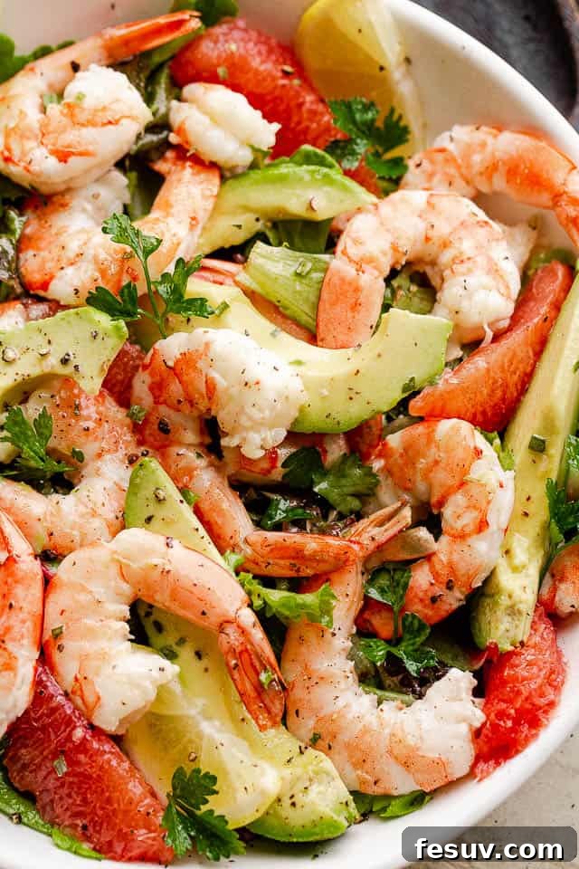 Cooked shrimp, vibrant avocado slices, and crisp salad greens are beautifully tossed together in a pristine white serving bowl, highlighting the freshness of this summer salad.