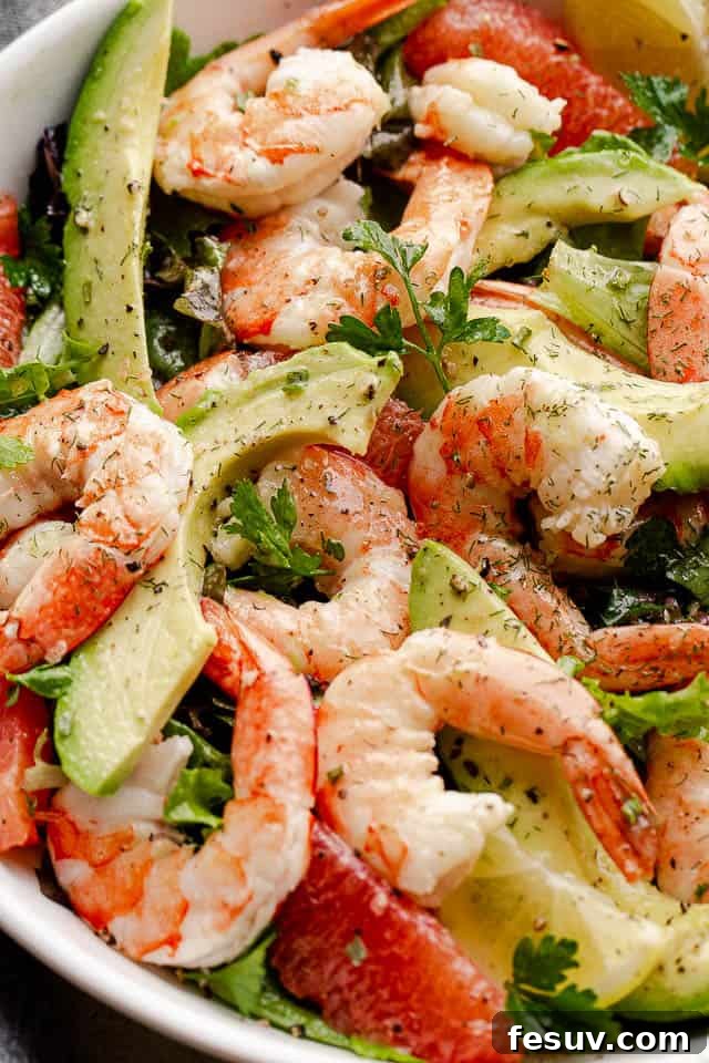 The same appetizing shot of cooked shrimp, avocado slices, and fresh salad greens arranged artfully in a white serving bowl, emphasizing its fresh appeal.
