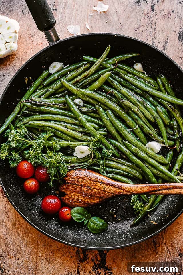 green beans, tomatoes, and garlic cloves in a black skillet with a wooden spoon inside