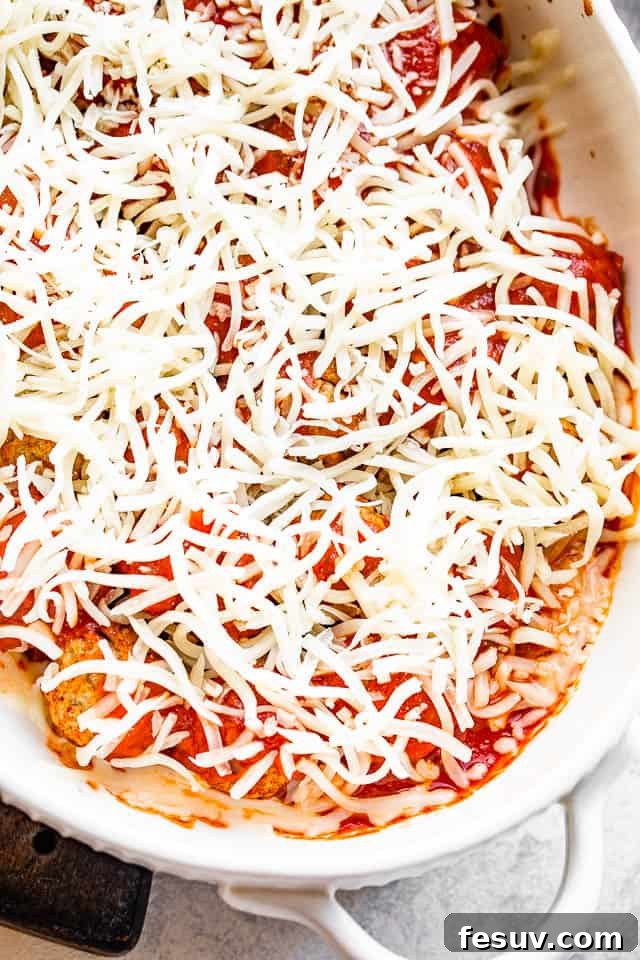 A casserole dish filled with baked meatballs, covered in vibrant marinara sauce, and topped with a generous layer of freshly shredded mozzarella cheese, poised for its final bake until bubbly and golden.
