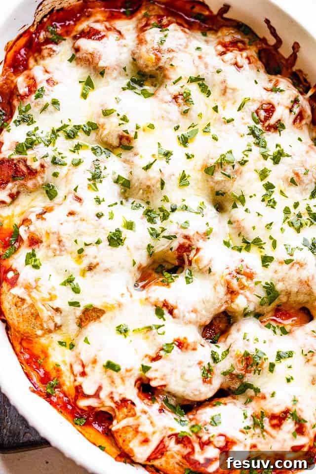 A close-up view of a baked meatball casserole in a white dish, showcasing the bubbling marinara sauce and a luscious, golden-brown layer of melted mozzarella cheese, indicating perfect readiness.