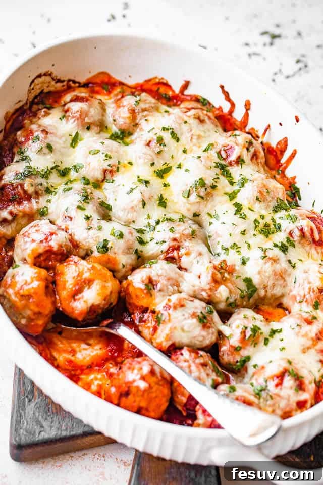 A pristine white baking dish filled with baked meatballs, luxuriating in rich marinara sauce and crowned with an irresistible layer of golden, melted cheese, ready for serving.