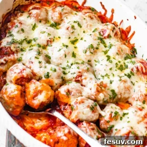white baking dish filled with baked meatballs covered in marinara sauce and melted cheese