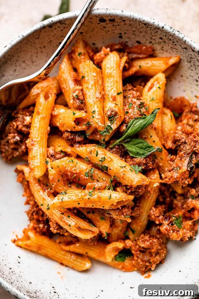 A bowl of freshly baked ziti pasta, rich with ground beef, vibrant tomato sauce, and three types of perfectly melted, gooey cheese, garnished with fresh basil.