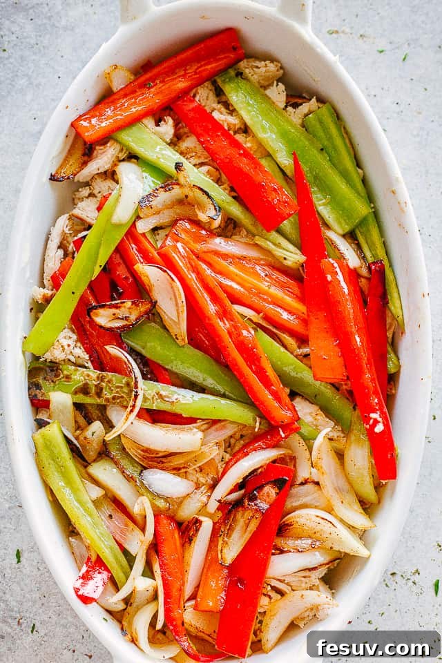 bell pepper strips arranged over shredded chicken in an oval baking dish