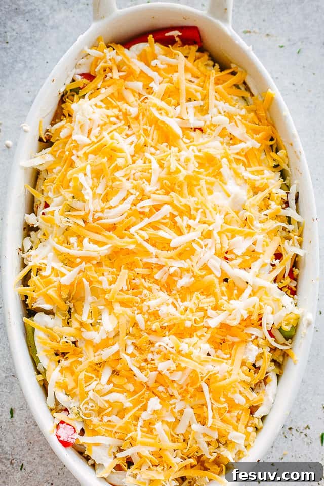 shredded cheese sprinkled over chicken and peppers in a white oval baking dish