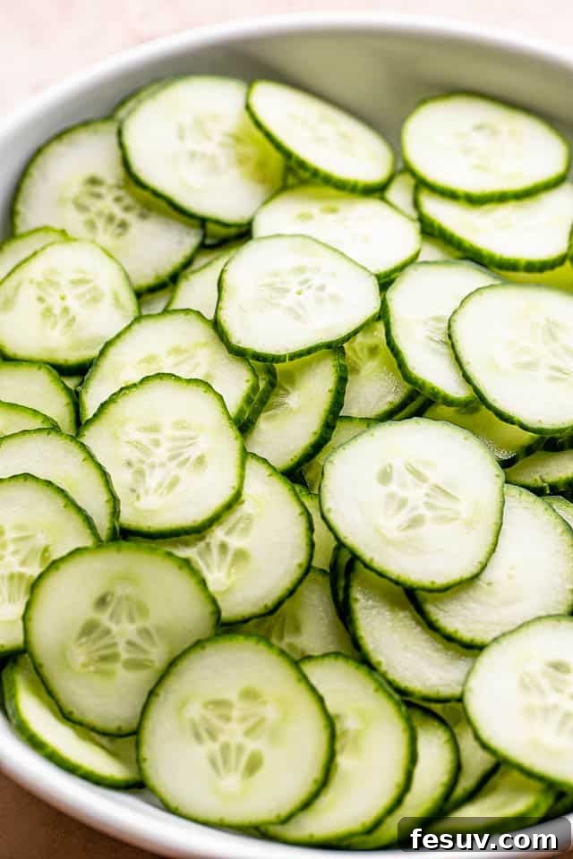 Close-up of thinly sliced English cucumbers neatly arranged in a white bowl, ready for the dressing.