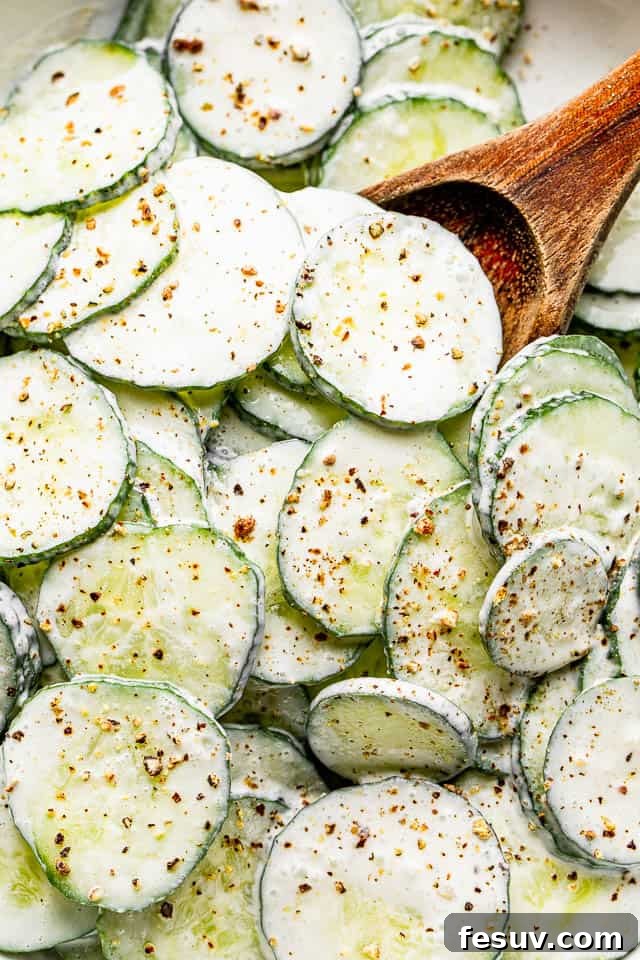 Top-down close-up shot of a wooden spoon scooping out a generous portion of cucumber salad from a white bowl.