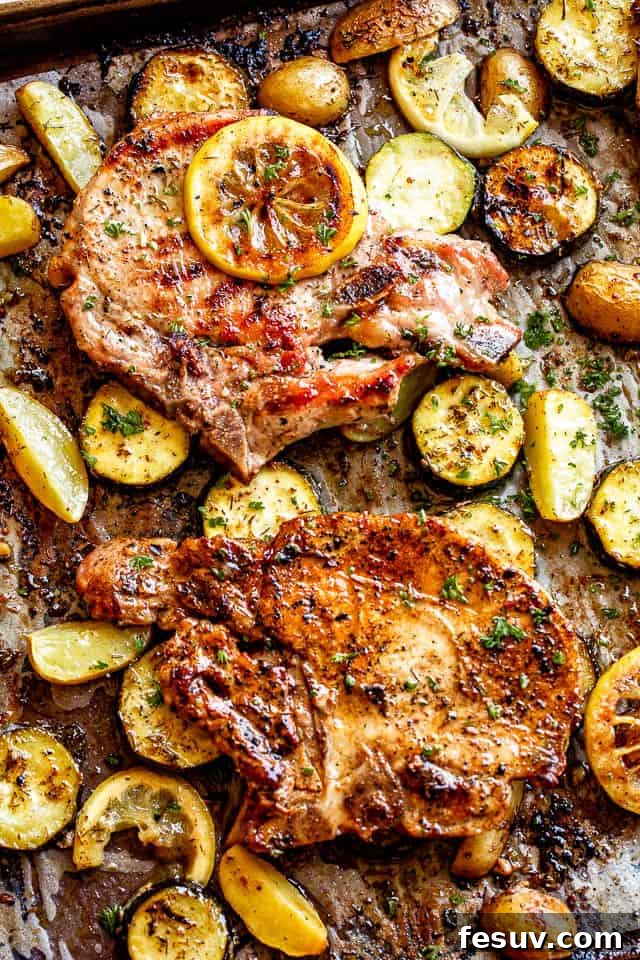 Sheet pan with perfectly baked lemon garlic pork chops resting on a bed of roasted squash and potatoes, garnished with fresh lemon slices.