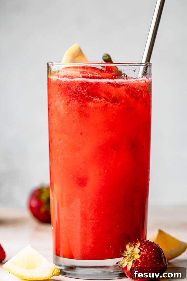 Pink Lemonade Berry Sangria 6 A tall glass brimming with luscious Strawberry Lemonade Sangria, showcasing its beautiful color and fresh fruit garnishes, awaiting enjoyment.