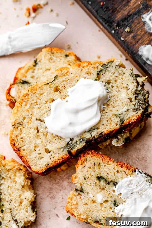 Close-up shot of a thick slice of spinach and feta no-yeast bread, topped with a dollop of creamy yogurt, showcasing its moist crumb and visible ingredients.