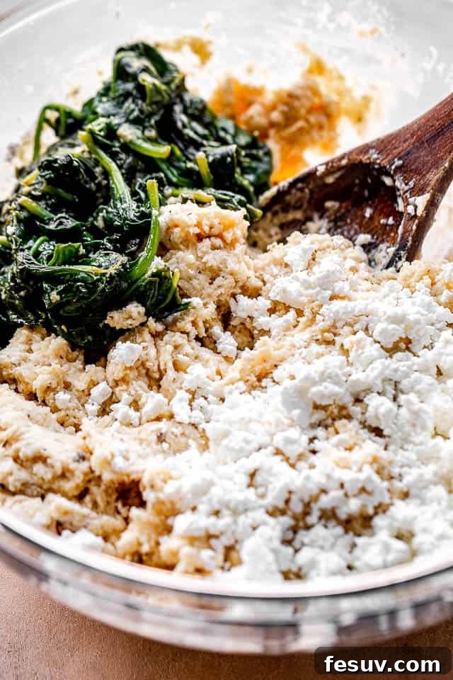 Side view of a large mixing bowl with wilted spinach, crumbled feta cheese, and all-purpose flour, ready to be combined.