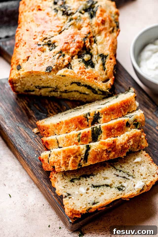 Top shot of sliced spinach and feta bread set on top of a dark cutting board, with sprigs of fresh rosemary for garnish.