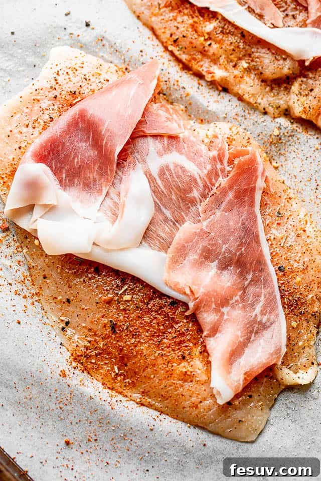 Slice of prosciutto set over a raw chicken breast, ready for rolling