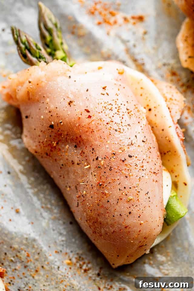 Raw chicken breast rolled up with asparagus spears and cheese slice, secured with toothpicks