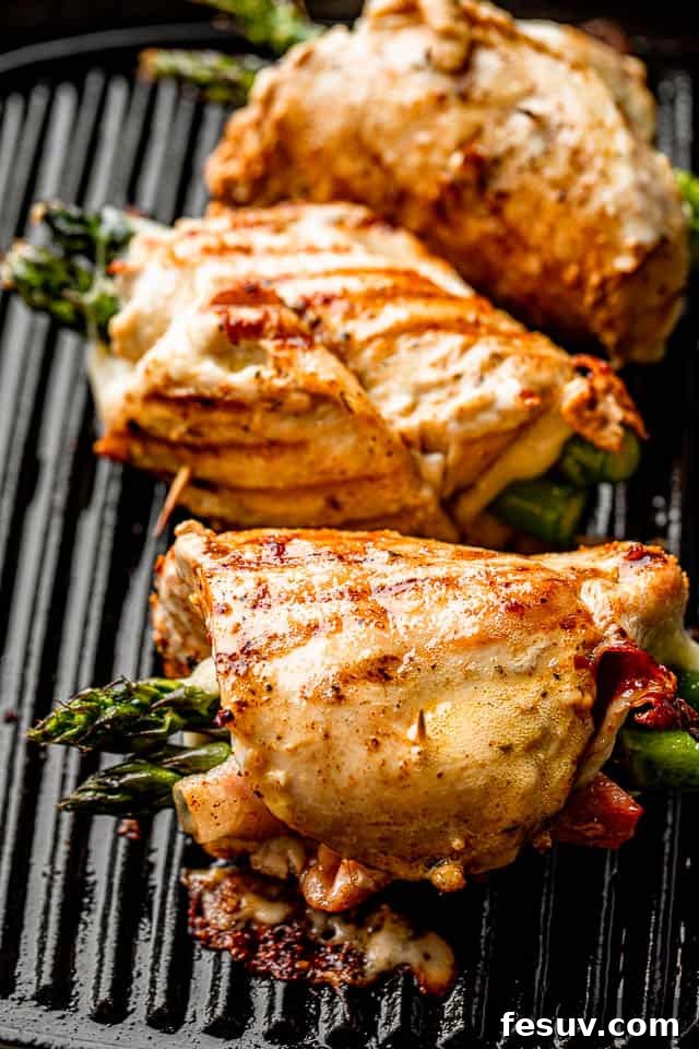 Three chicken roll ups stuffed with asparagus, prosciutto, and cheese, cooking on a grill pan, with a golden crust