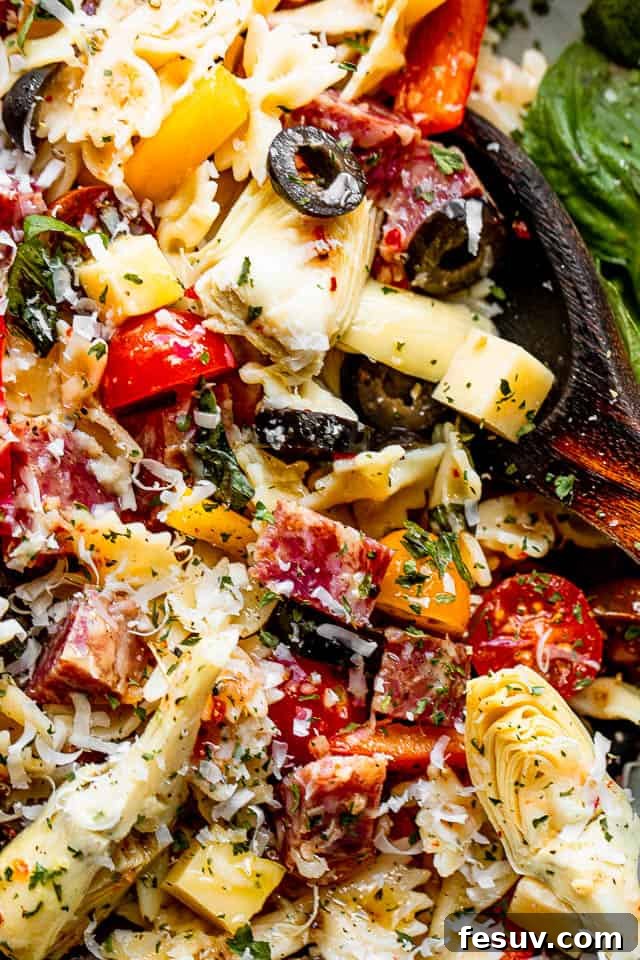 Vibrant Italian Antipasto Pasta Salad close up shot of a salad bowl filled with pasta, cheese cubes, salami cubes, tomatoes, and olives