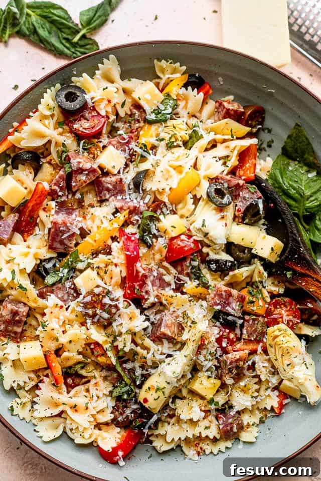 Ready-to-Serve Italian Pasta Salad top view shot of a wooden spoon in a bowl filled with pasta, cheese cubes, salami cubes, tomatoes, and olives