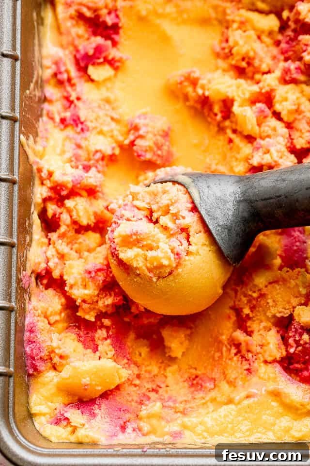 close up shot of mango strawberry frozen yogurt in a loaf pan with an ice cream scoop