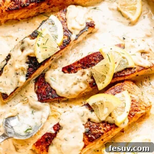 white pan with four salmon fillets topped with lemon slices and cream sauce