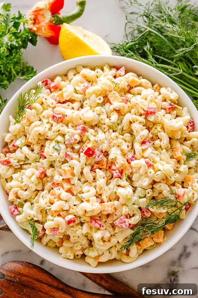 Bowl of creamy macaroni salad, garnished with fresh herbs.