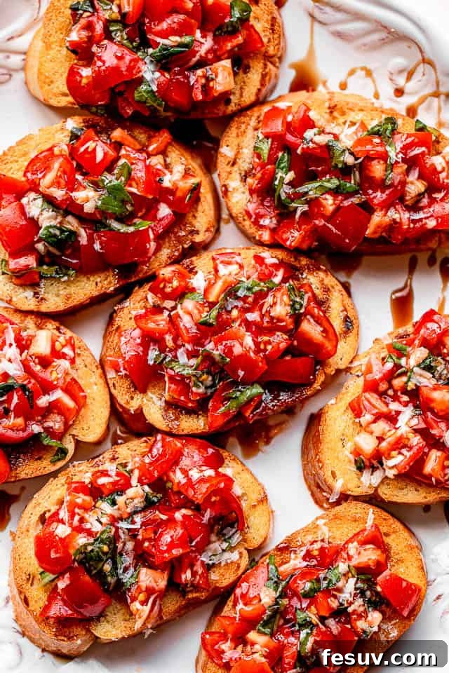 Crispy garlic bread slices generously topped with a fresh tomato and basil salad, arranged on a white serving platter.