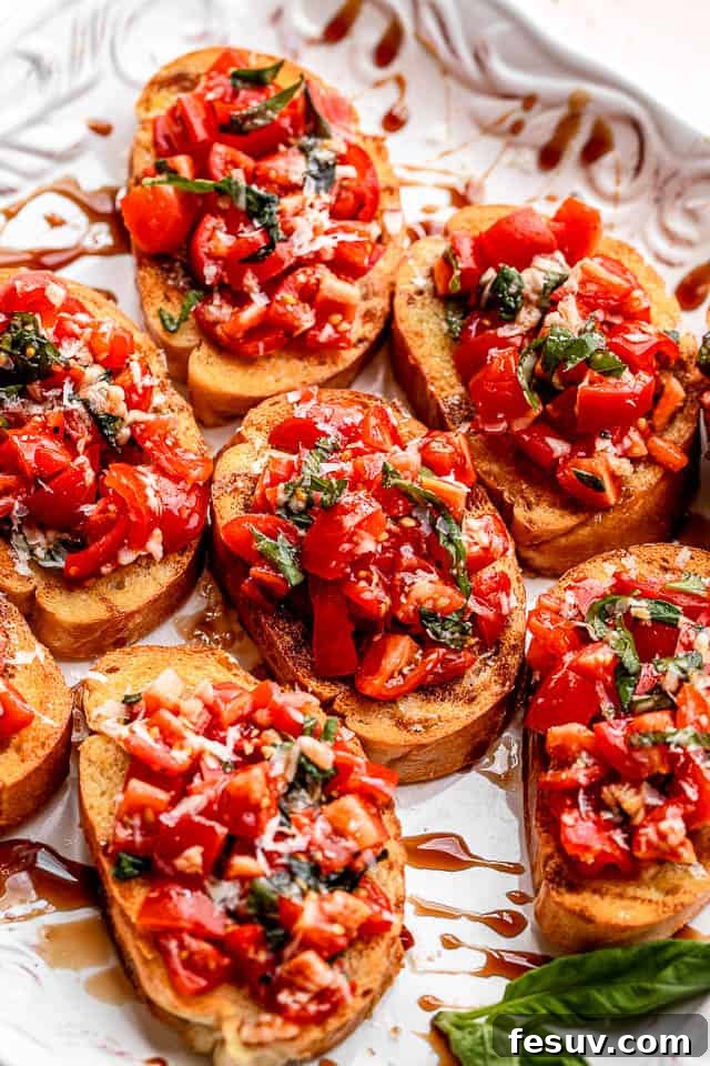 A elegant white platter showcasing multiple pieces of garlic bread bruschetta, artfully topped with a fresh tomato salad and drizzled with a rich balsamic glaze.