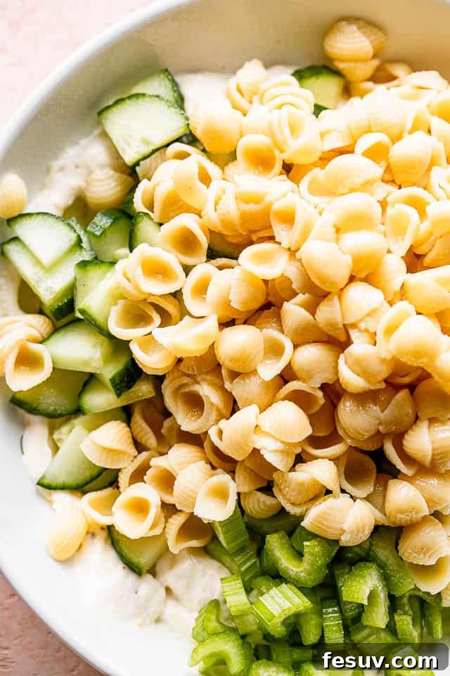 Small pasta shells set over diced cucumbers and celery in a white bowl