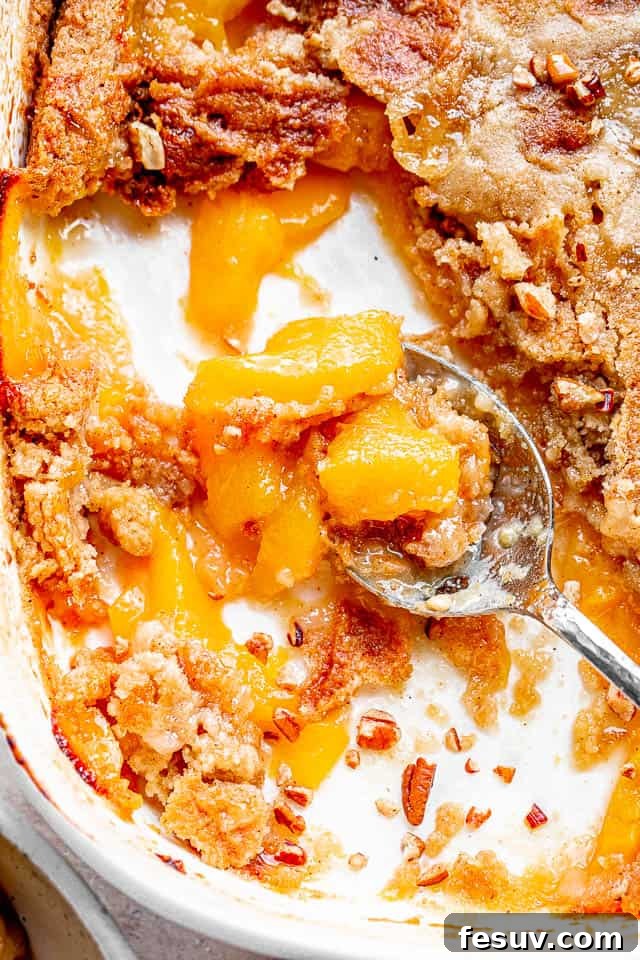 top shot of silver spoon scooping out a peach cake from white baking dish