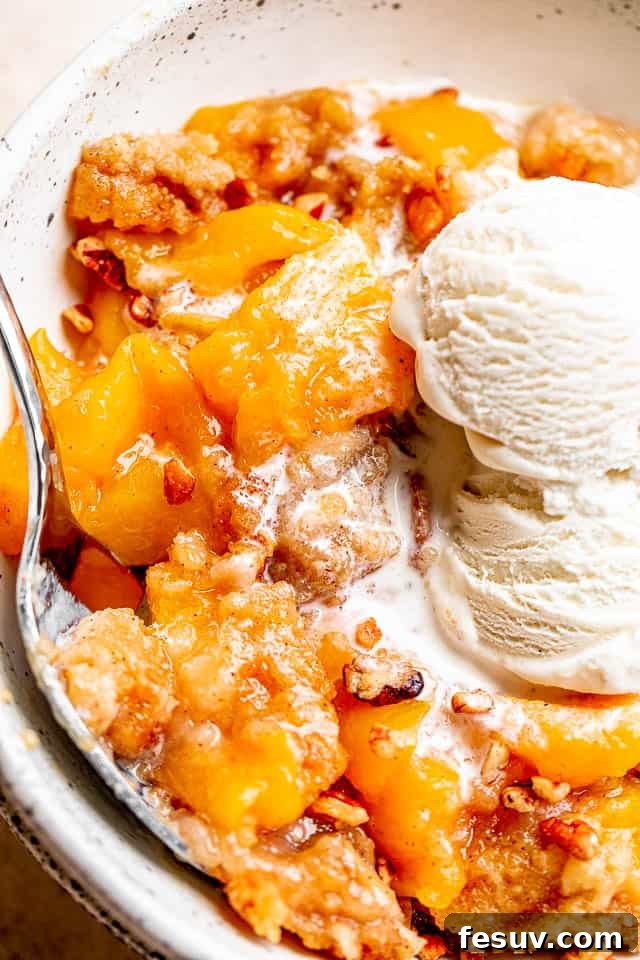 Side shot of a bowl with peaches and cake and vanilla ice cream.