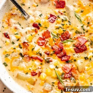 Silver spoon inside a bowl of creamy Instant Pot Corn Chowder, topped with crispy bacon, green onions, and parsley.