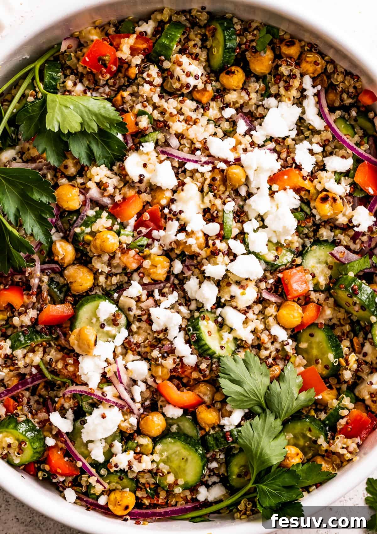 Close up shot of a salad with chickpeas, sliced cucumbers, red onions, peppers, herbs, and feta.