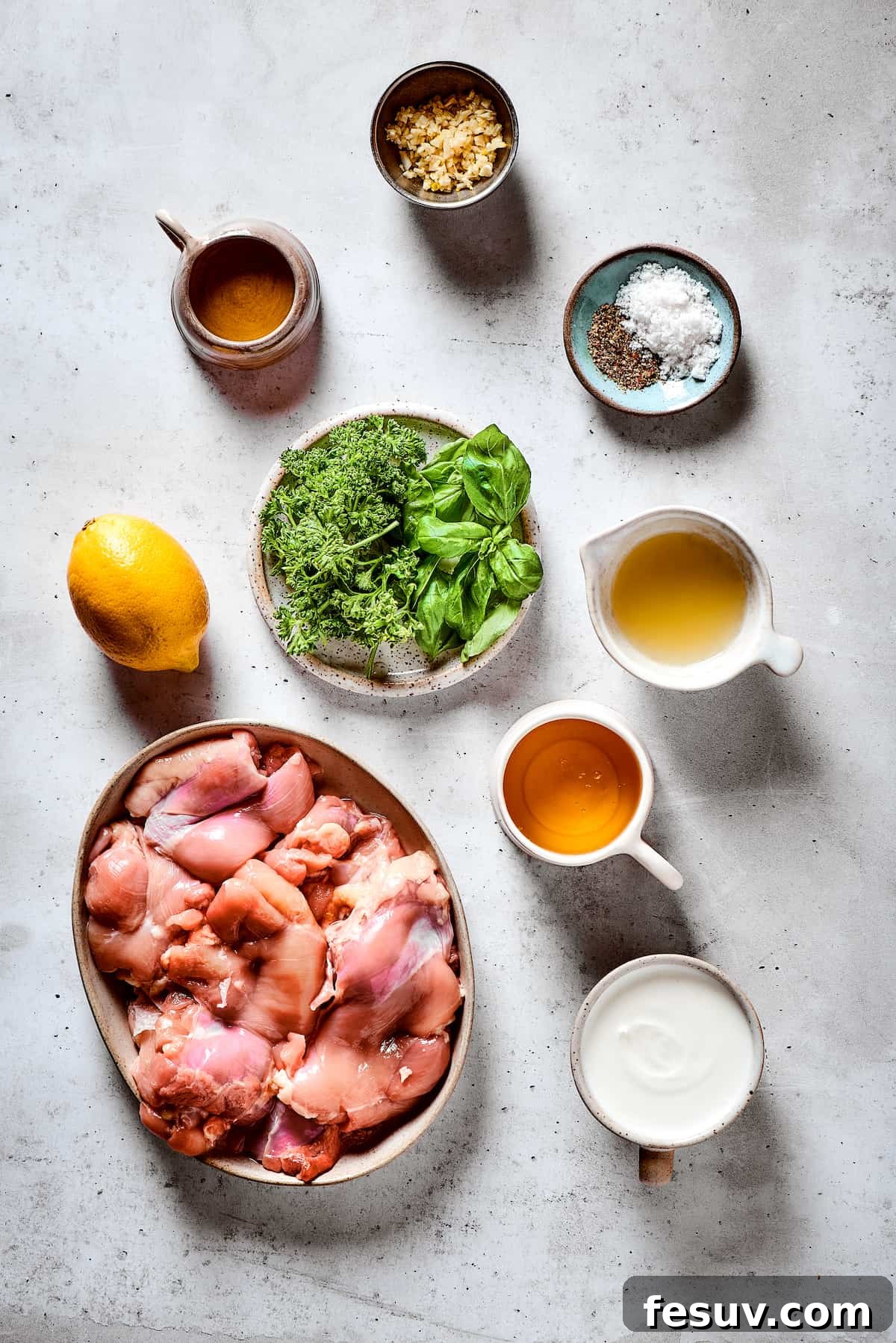 Yogurt Marinated Chicken is an easy grilled chicken recipe that’s versatile, zesty, and easy to make. Everyone will rave over this easy dish! An overhead flat lay showcasing all the fresh ingredients for yogurt marinated chicken: garlic cloves, salt and pepper, vibrant lemon juice, golden honey, creamy yogurt, raw chicken thighs, fresh herbs, and olive oil.