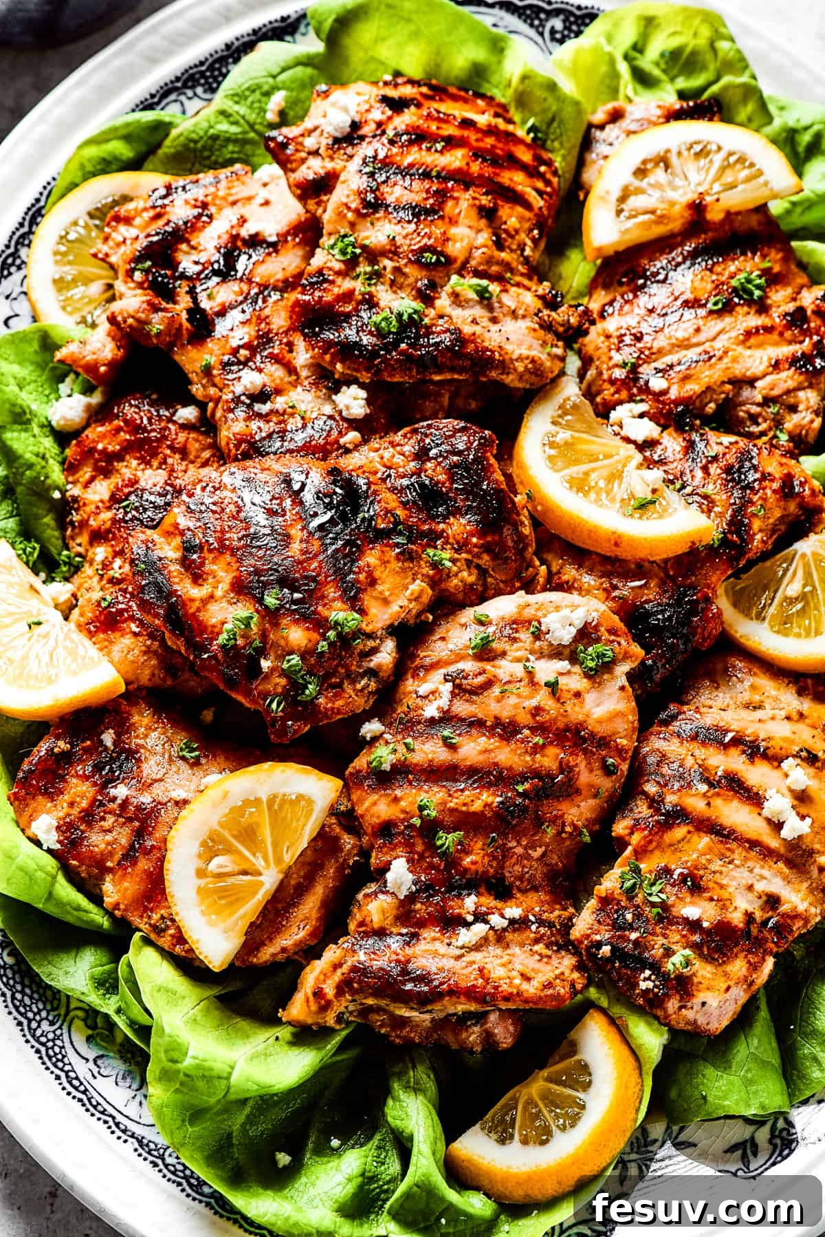 Yogurt Marinated Chicken garnished with feta cheese. A close-up of grilled yogurt-marinated chicken, glistening with juices, topped with crumbled feta cheese and fresh herbs, served on a bed of vibrant lettuce leaves.